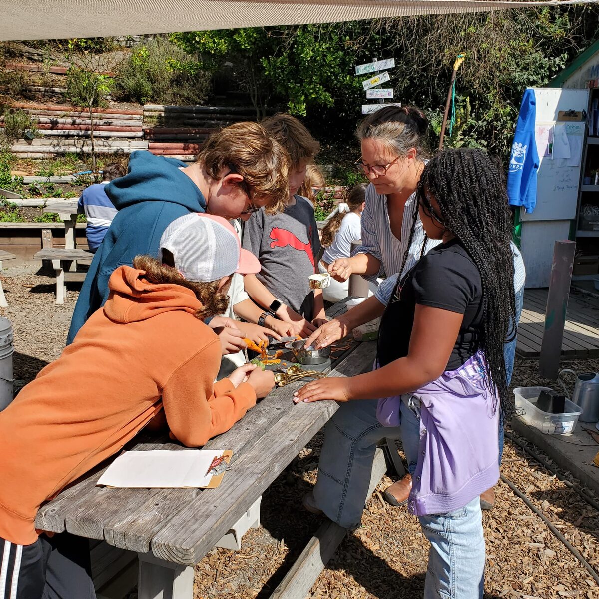 Madera students and a teacher preparing vegetables together at a picnic table in the school garden